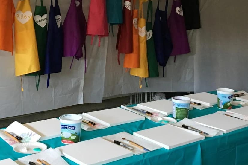Paint party table setup with canvases, brushes, and personalized colorful aprons