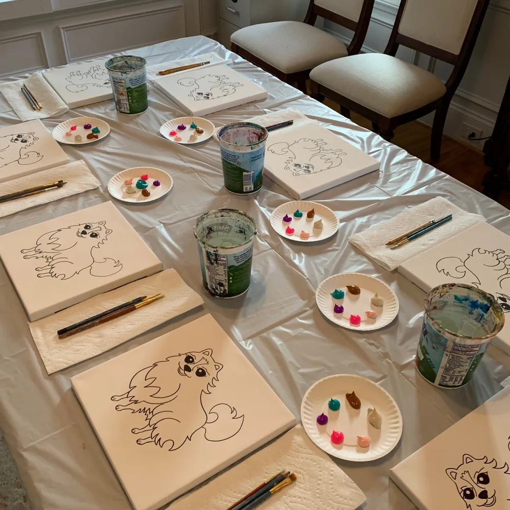 Dining table set with pre-sketched puppy canvases, paper plate palettes, water cups, and brushes for a kids painting party in Alpharetta, GA