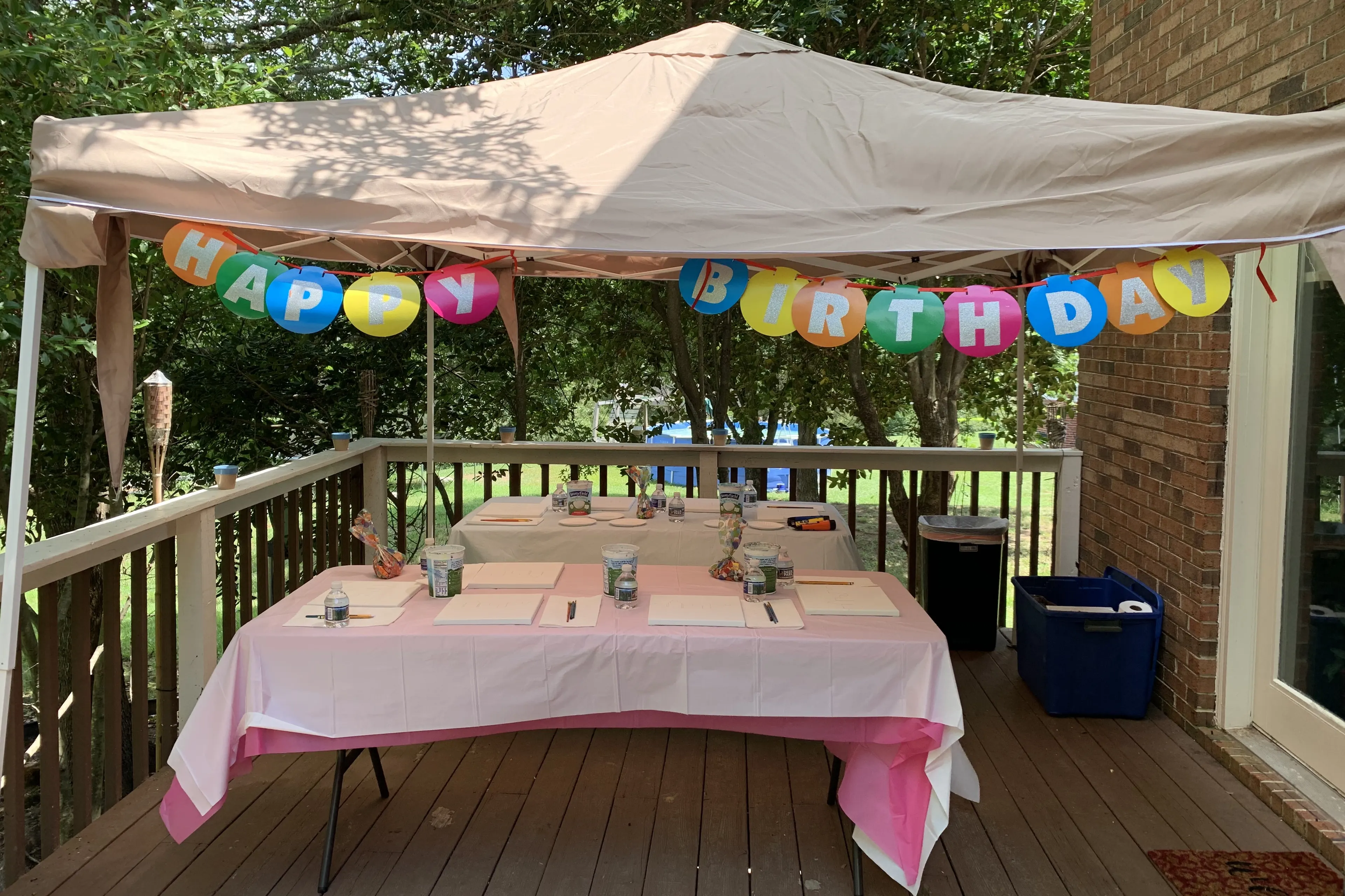 Outdoor kids paint party setup under a tent with a birthday banner, blank canvases, and paint supplies