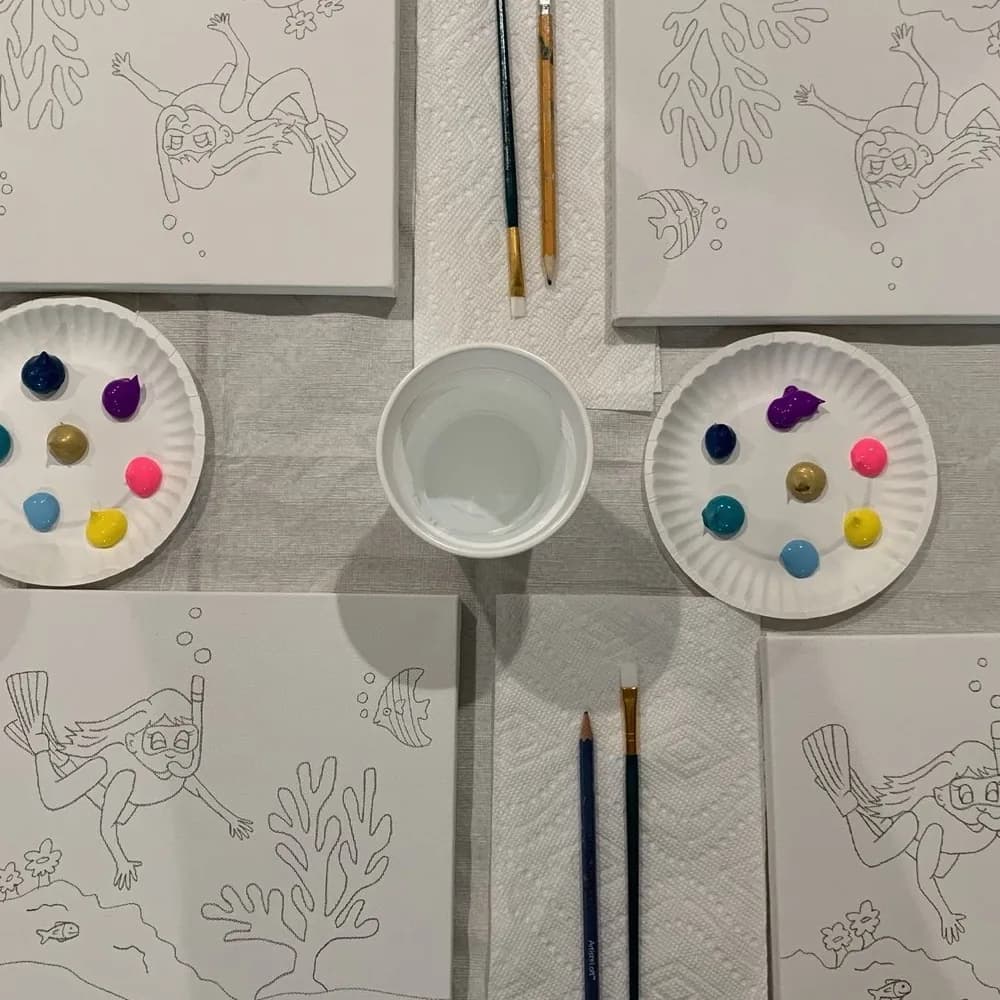 Party table set with pre-sketched snorkeler canvases, paint plates, water cups, and brushes for a kids painting party in Katy, TX