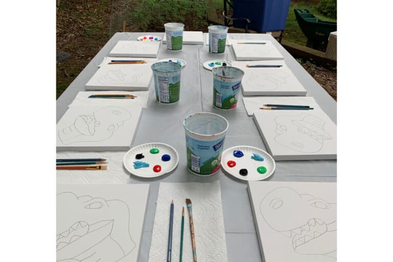 Outdoor paint party setup with pre-sketched dinosaur canvases and supplies
