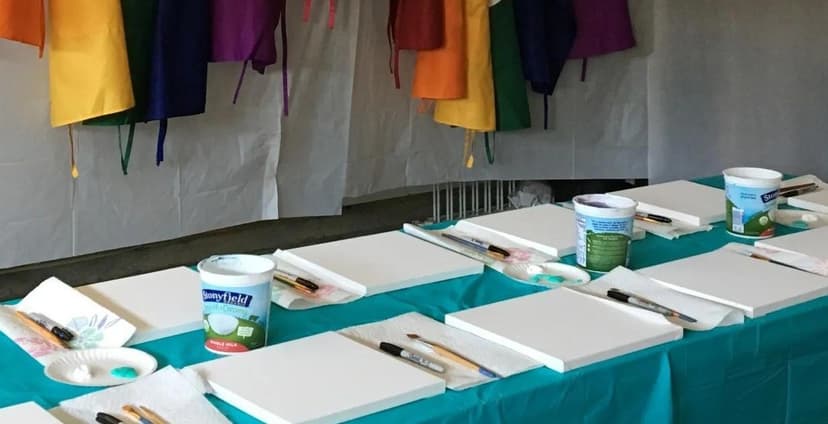 Paint party table setup with canvases, brushes, and colorful aprons