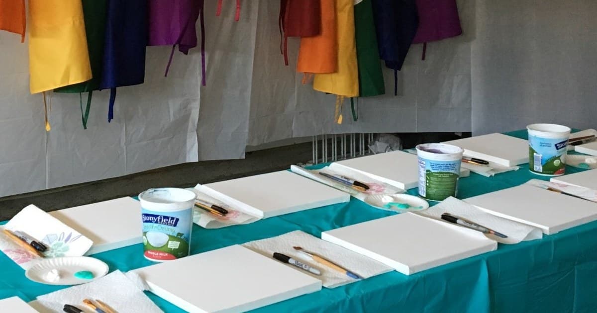 Paint party table setup with canvases, brushes, paint, and colorful aprons