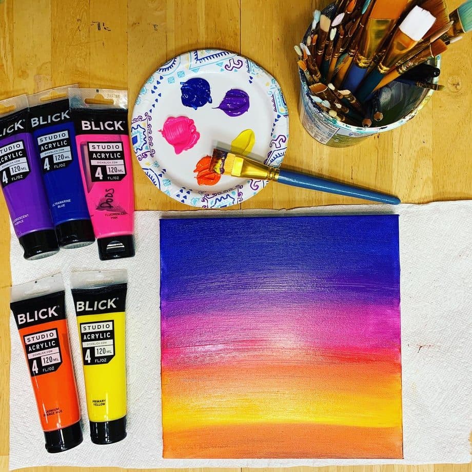 Acrylic paint tubes, brushes, and a finished sunset canvas painting